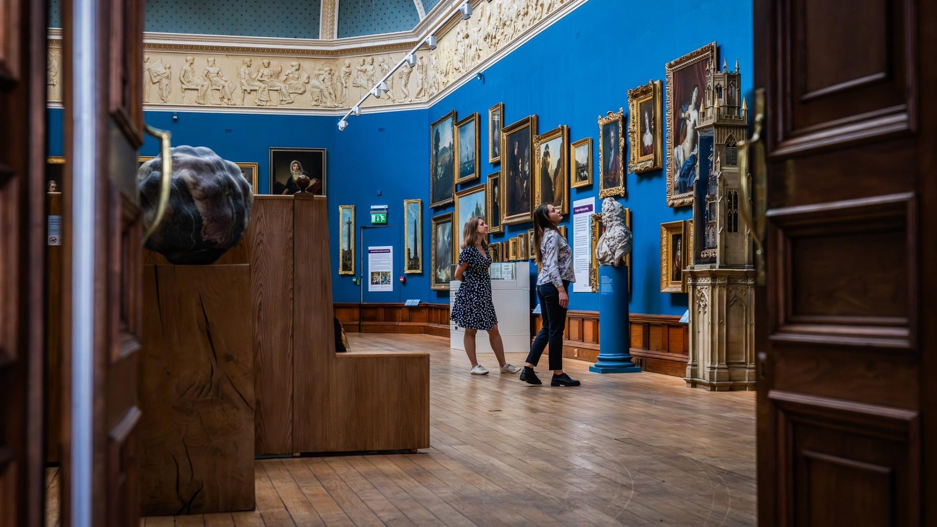 Two people browsing the exhibits in the Upper Gallery at the Victoria Art Gallery in Bath.