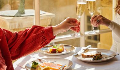 Two guests cheers with glasses of Champagne and starter plates in the Pump Room