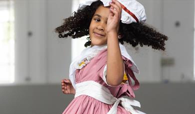 A little girl wearing a red dress with a white hat