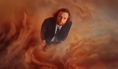 Man in a pinstripe suit stands amid swirling orange and grey cloud-like textures. 