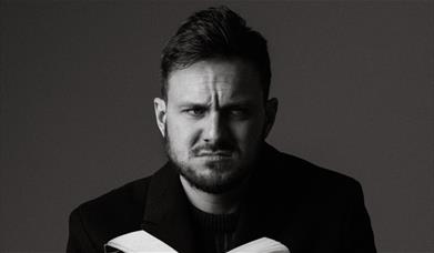 Black and white potrait of Mike Rice holding an open book and staring intensely at the camera. 