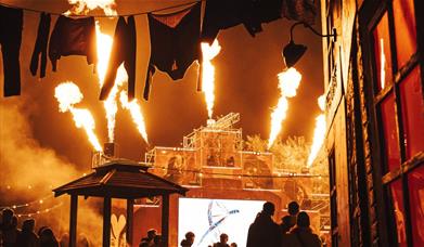 Fire show at Avon Valley FEAR event, with jets of flame erupting from the top of a tall stage in several directions.