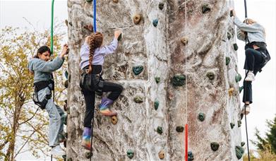 Three children attached to ropes and harnesses scaling a climbing wall