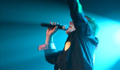 A photo of the singer for Tribute Triple Bill singing into a microphone 