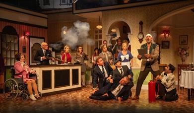 A scene from Fawlty Towers the play, containing most of the cast during a comedic moment.