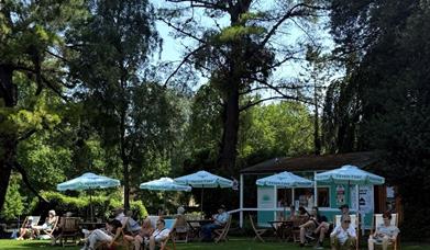 Customers enjoy the House of Friends park cafe, sat on deckchairs under parasols in the Parade Gardens park