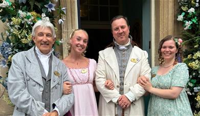 Four staff members dressed in regency clothing stand outside the entrance to the Jane Austen Centre.