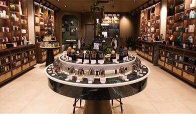 A luxurious store interior, with ceiling-high shelves on either side of the room and a circular unit in the centre all displaying bottled products