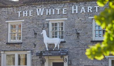 A stone building with The White Hart written on the front in white lettering and a large white stag statue above the door 