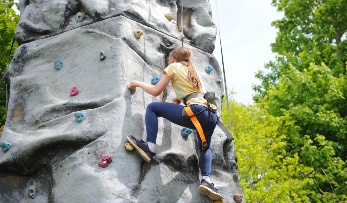 A young girl wearing blue leggings and a yellow t shirt on a climbing wall