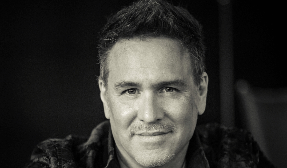 A black-and-white portrait of a smiling man with short greying hair.