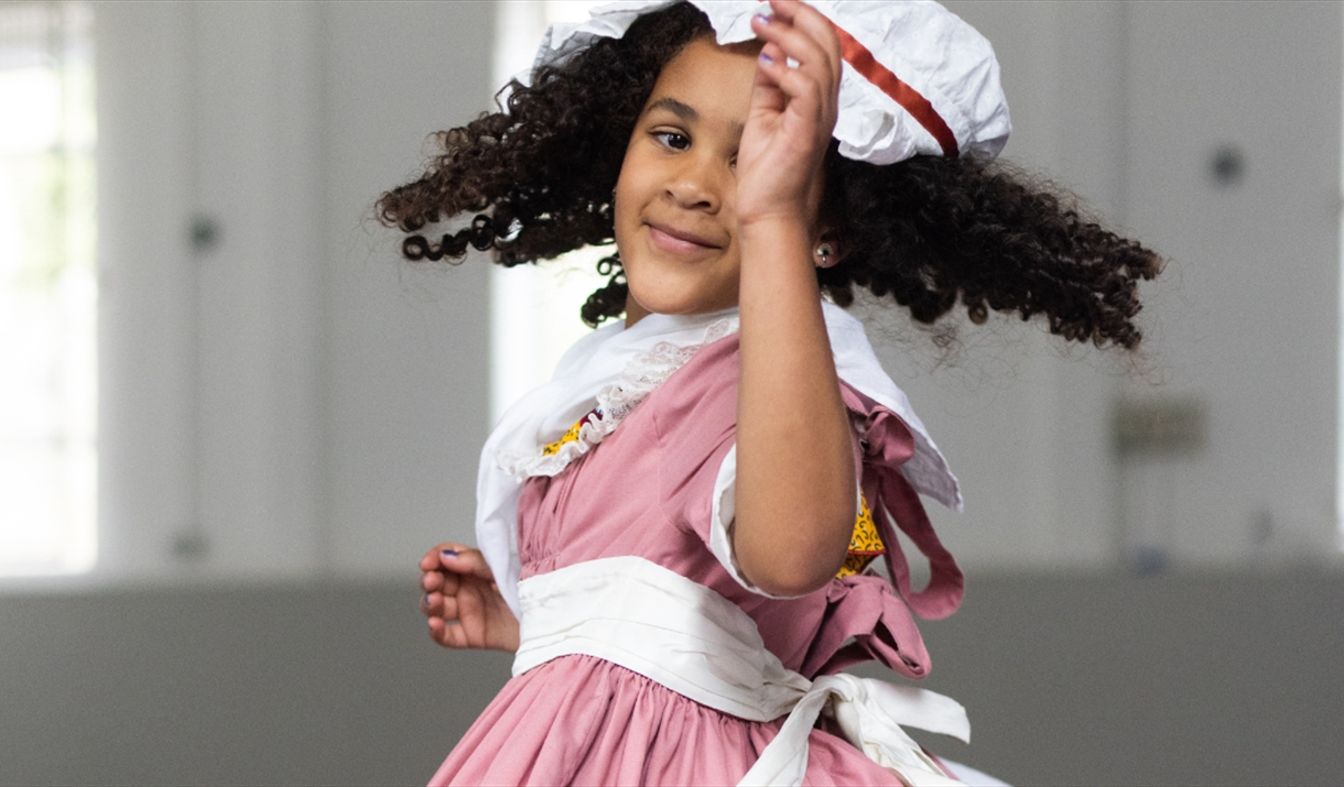 A little girl wearing a red dress with a white hat