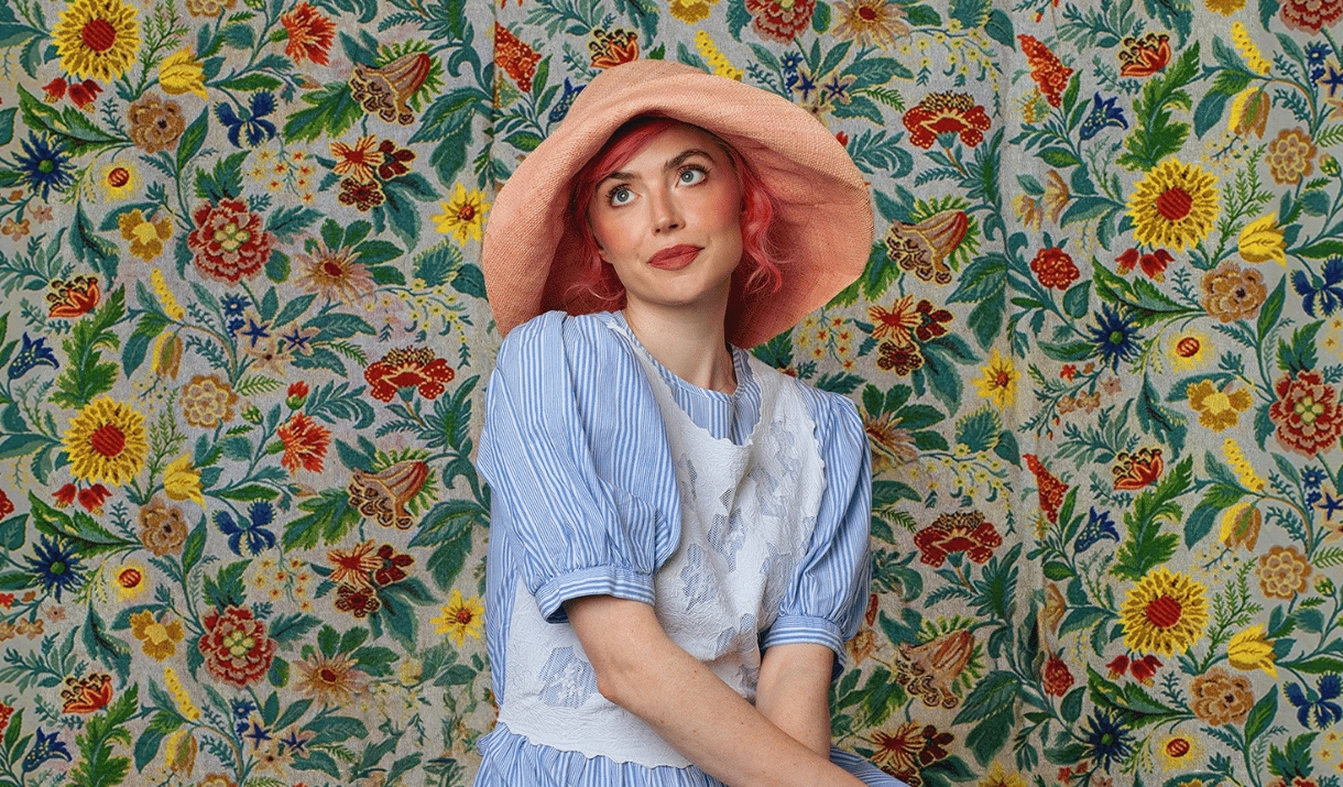 Woman in a pink sun hat posing against a colourful floral wall.