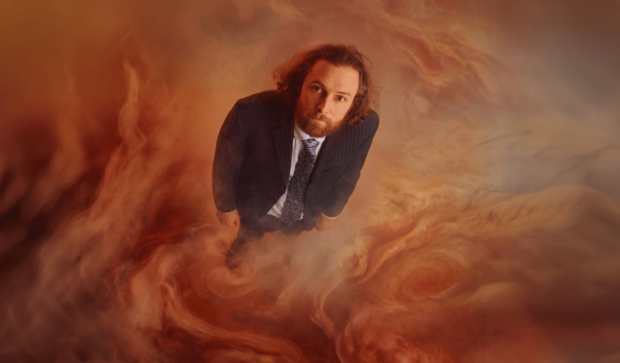 Man in a pinstripe suit stands amid swirling orange and grey cloud-like textures.