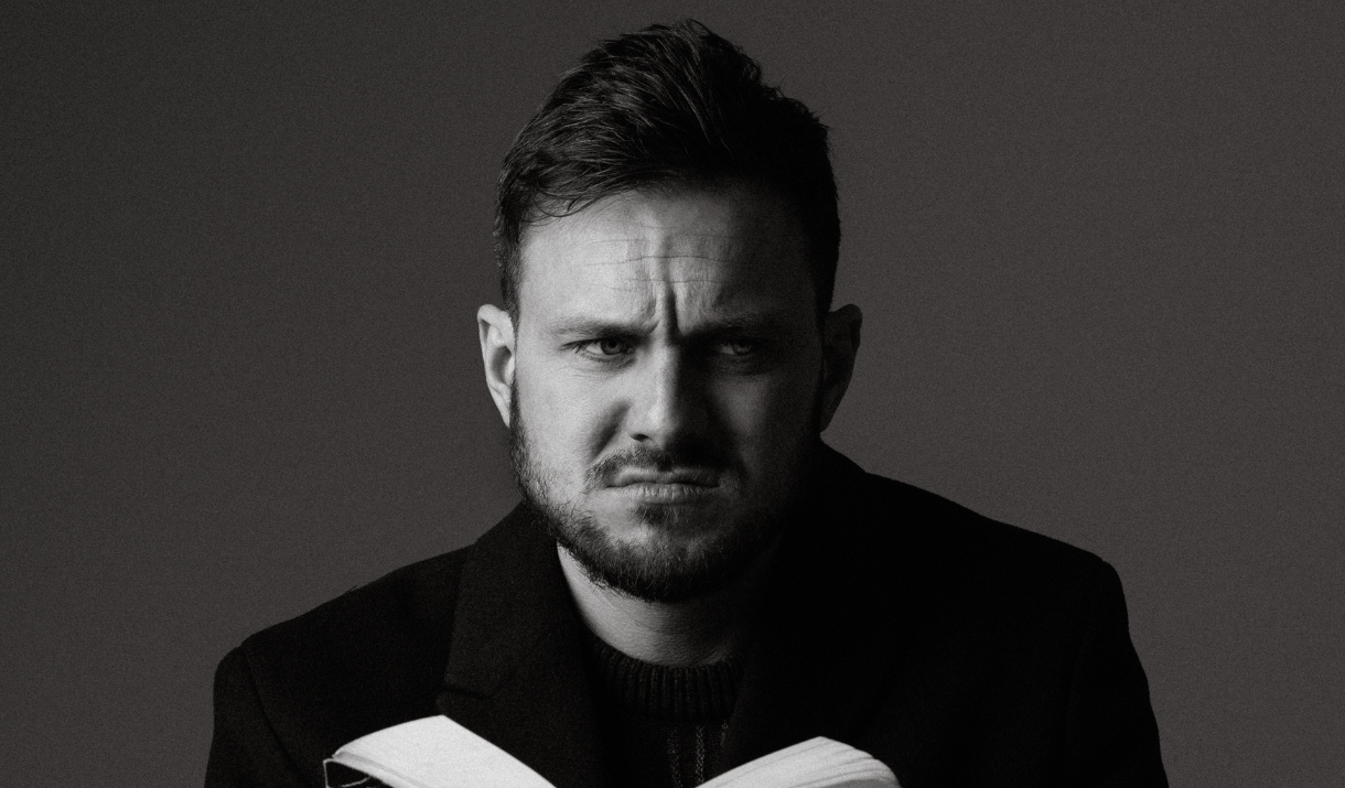 Black and white potrait of Mike Rice holding an open book and staring intensely at the camera.