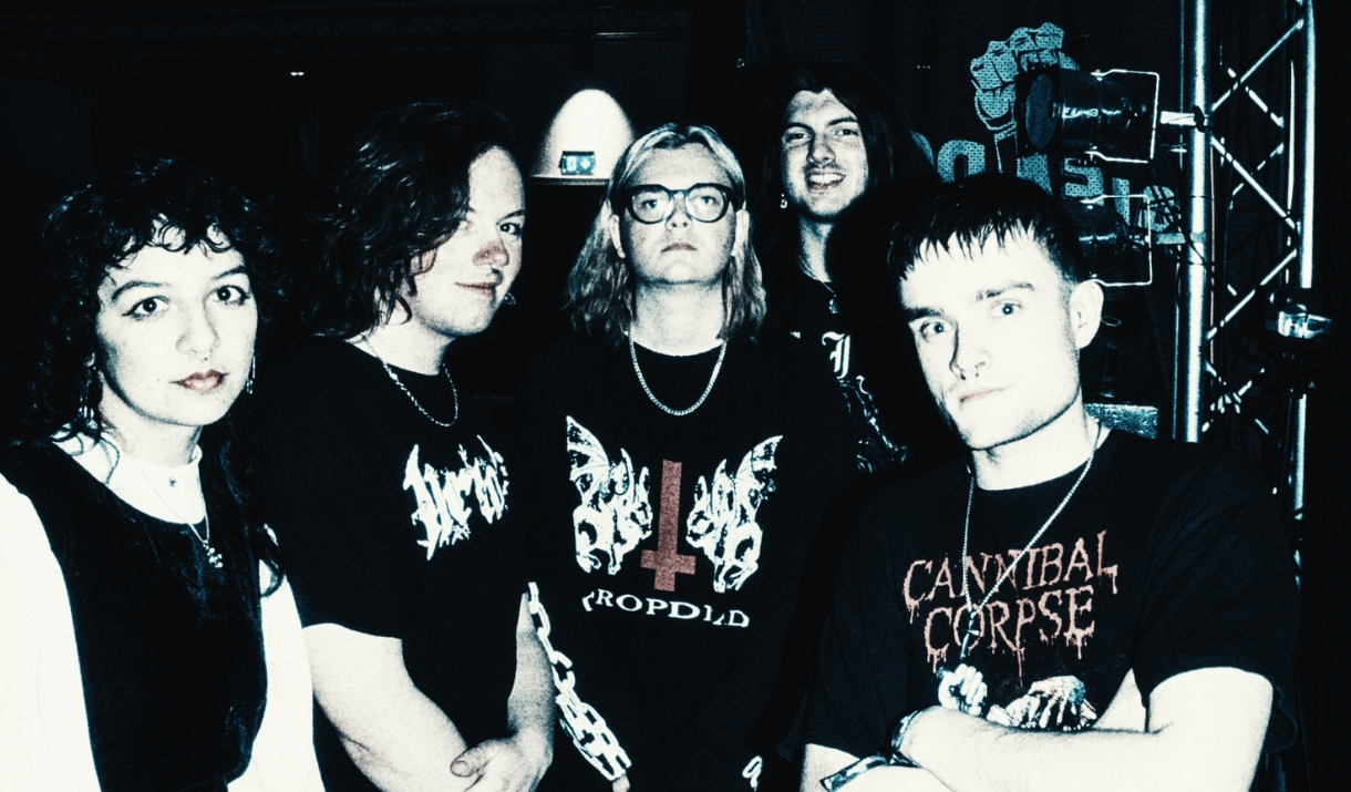 Band photo of five young people backstage in dark, moody lighting, wearing black metal-band t-shirts.