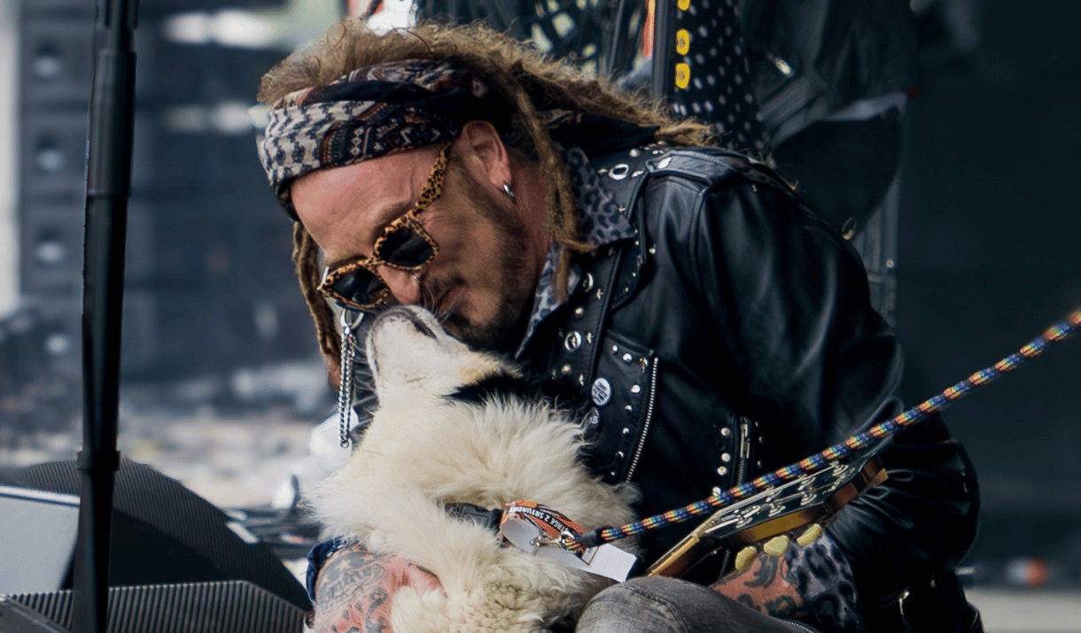 A rock musician in a studded leather jacket cuddles a fluffy dog on stage.