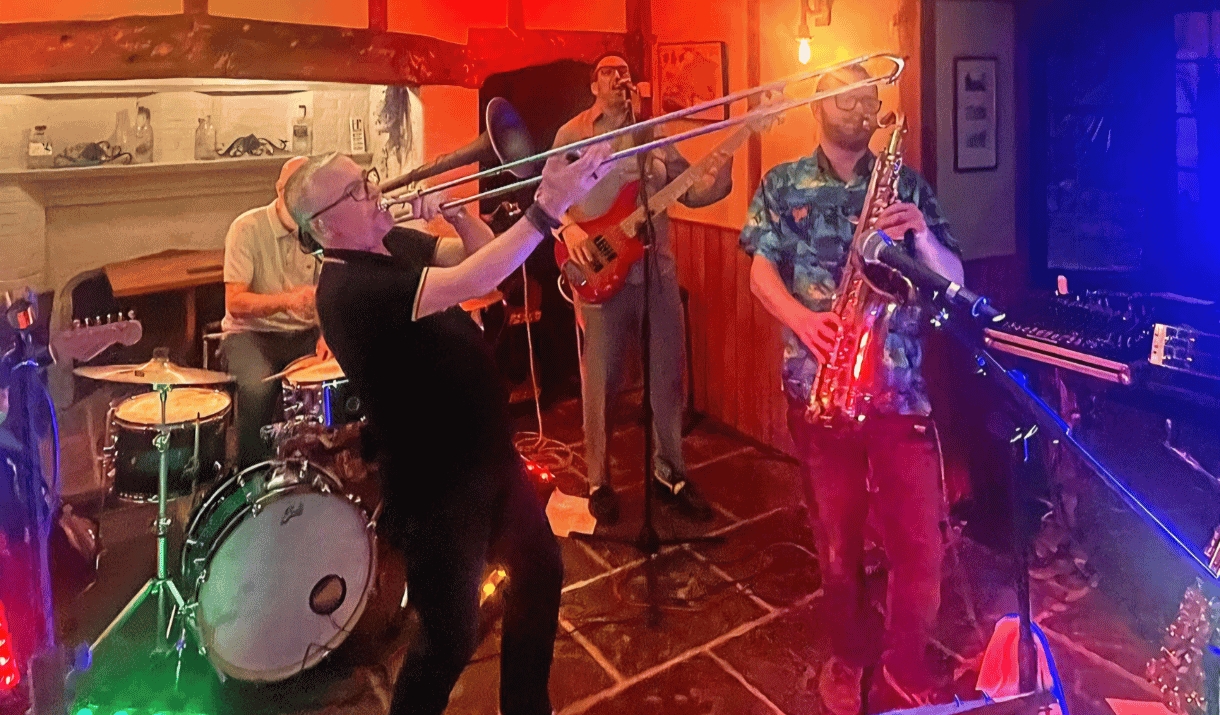Photo of a band performing in a venue. With colourful lighting, a trumpet, saxophone, guitar and drum kit.