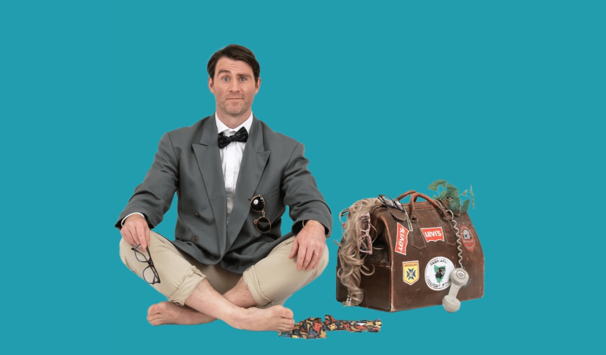 Jimmy Rees sat cross-legged in a bow tie and blazer beside a battered, sticker-covered suitcase.