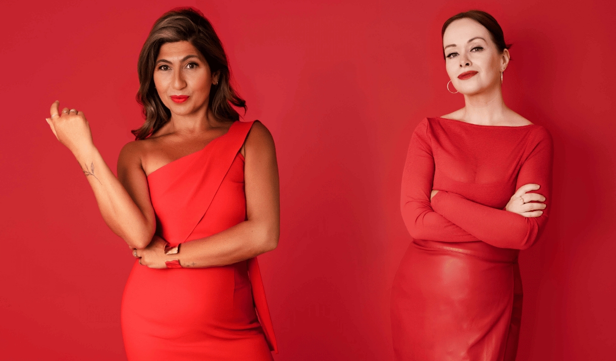 Two women in red outfits pose confidently against a red backdrop.