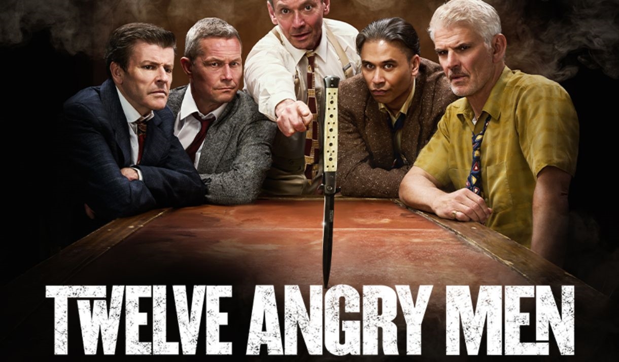 5 men stand around a table with a knife in the middle.