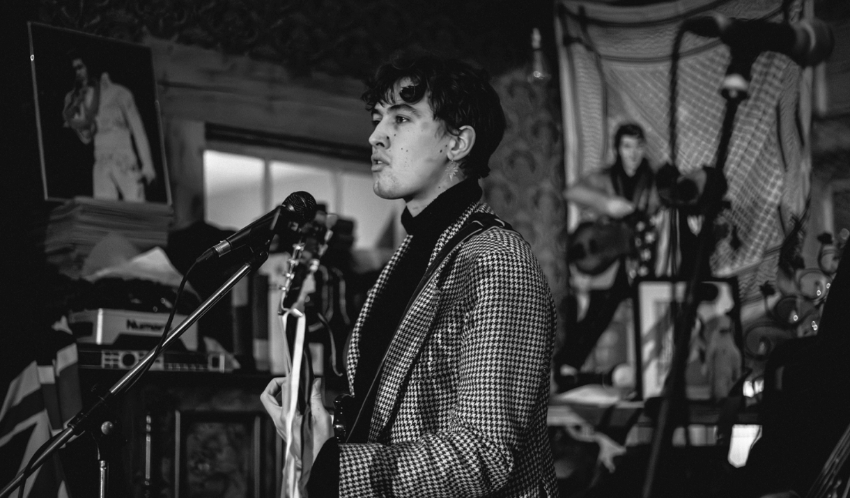 Photo of a band performing in a venue. Two men holding guitars and one with a microphone.