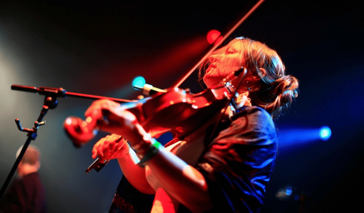 A woman plays the violin on stage, lit in vivid red and blue lighting.