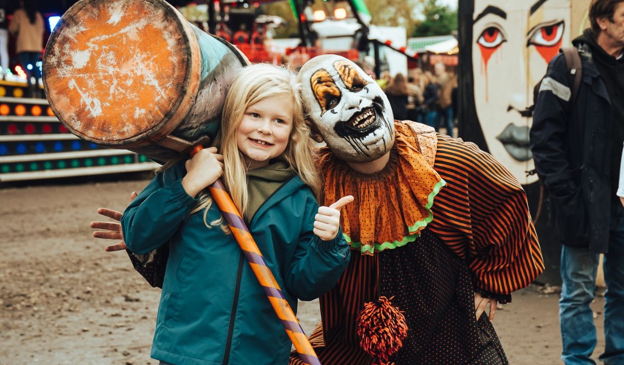 A child posing for the camera alongside a creepy clown with a large mallet.