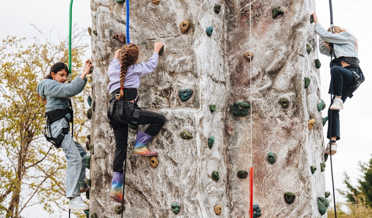 Three children attached to ropes and harnesses scaling a climbing wall
