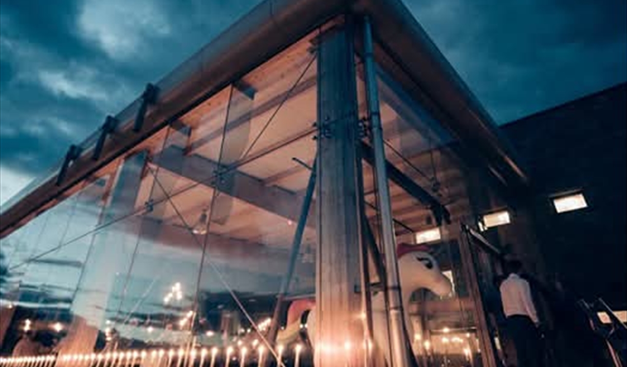 A night time image of the side of Boann distillery. The side of the distillery is all glass allowing a view into the shiny copper stills inside.