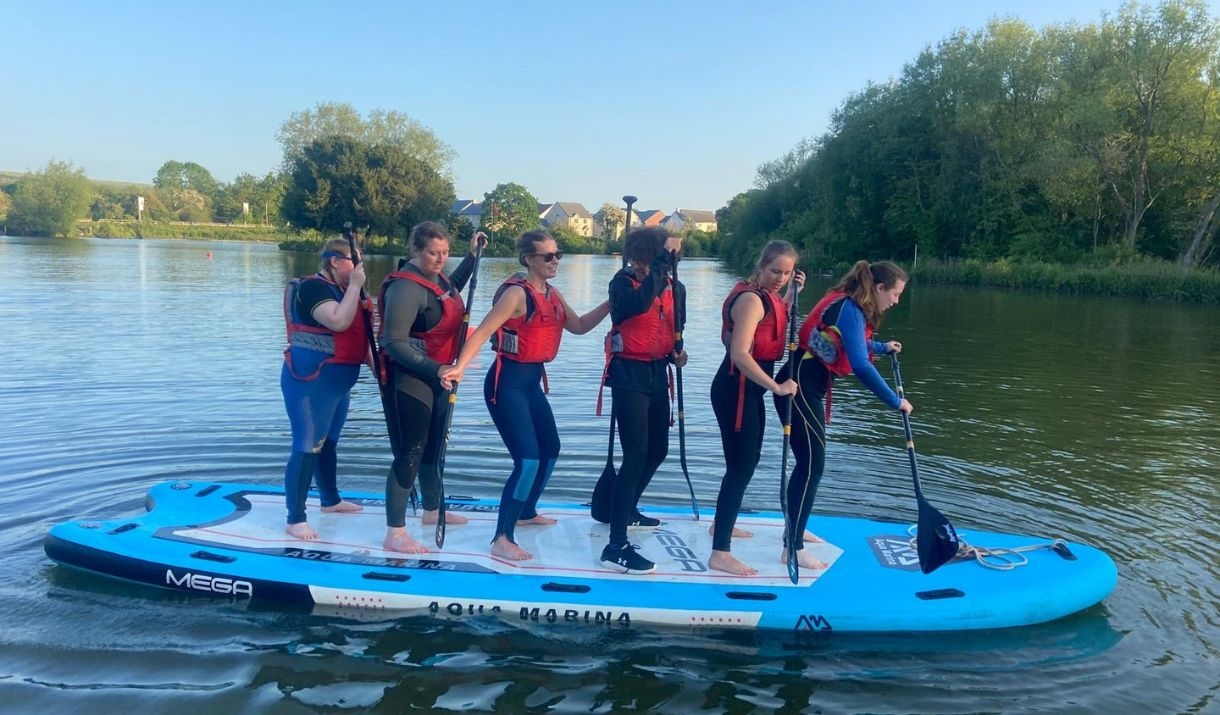 Photo of a group of people on a group paddleboard having fun afloat.