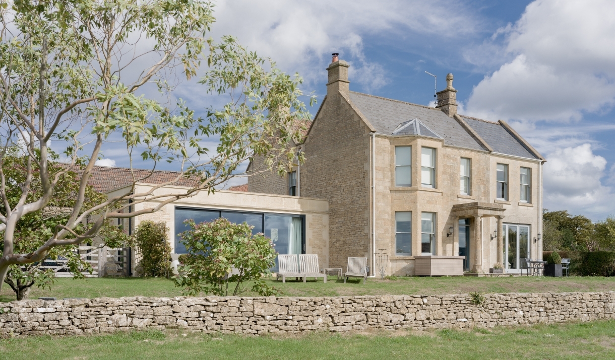 The exterior of Merryfields, a large modern cottage with a low stone wall in front.