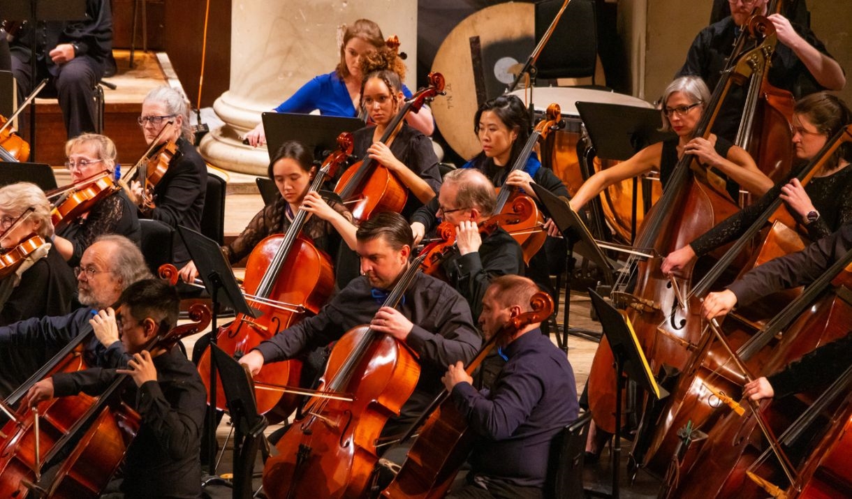 Orchestra members standing with their conductor