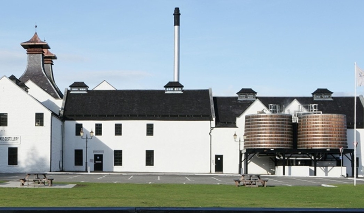 An image of Dalwhinnie distillery focused on the that  walls of the distillery are bright white and it is a clear sunny day.almost the size of the wal