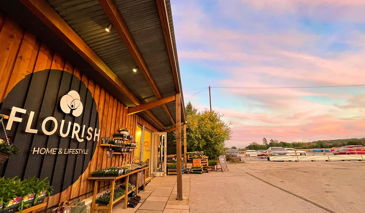 The outside of Flourish home and lifestyle shop timber building with a pink sky and car park in background