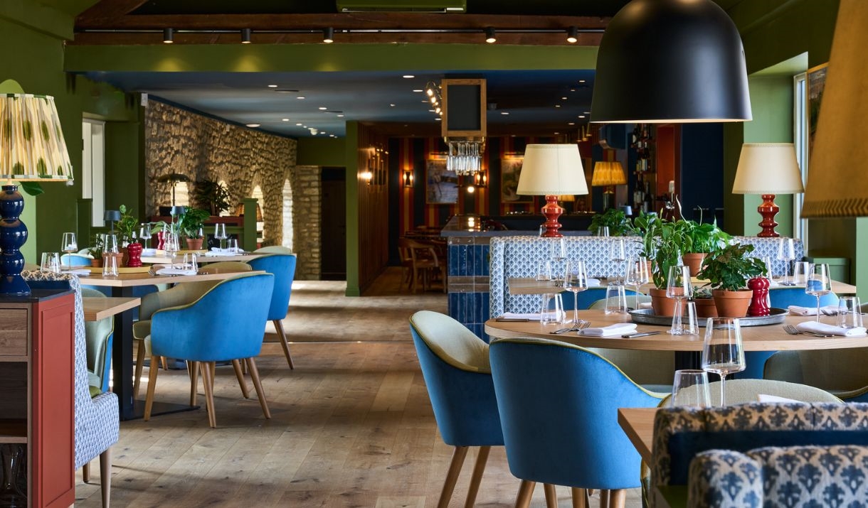 Restaurant with blue chairs, wine glasses, potted plants on tables.