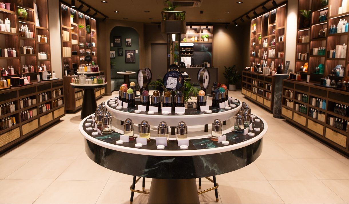 A luxurious store interior, with ceiling-high shelves on either side of the room and a circular unit in the centre all displaying bottled products