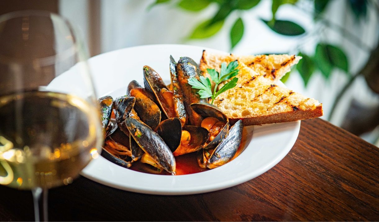 A plate of mussels and garlic bread with a glass of white wine.