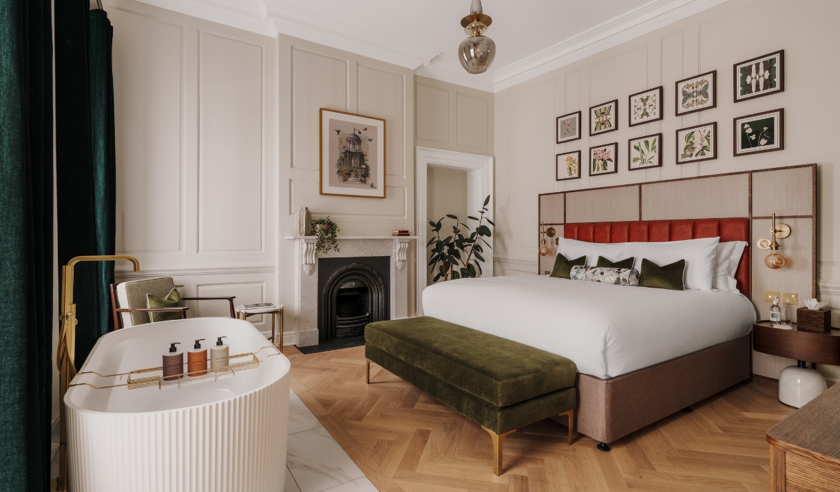 Highly spec'ed bedroom with oak parquet flooring, a green velvet ottoman and free standing bath at the end of a double bed with a Victorian fireplace.