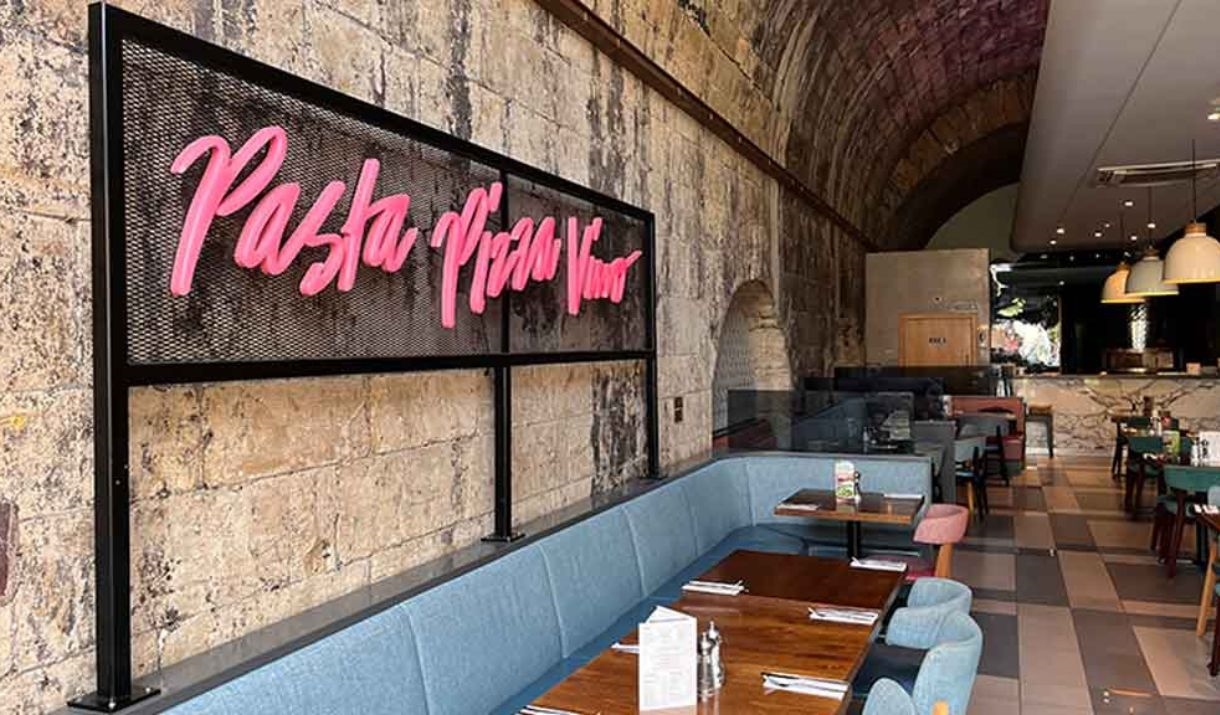 Pink signage alongside the dining area at Prezzo Bath reads "Pasta Pizza Vino"