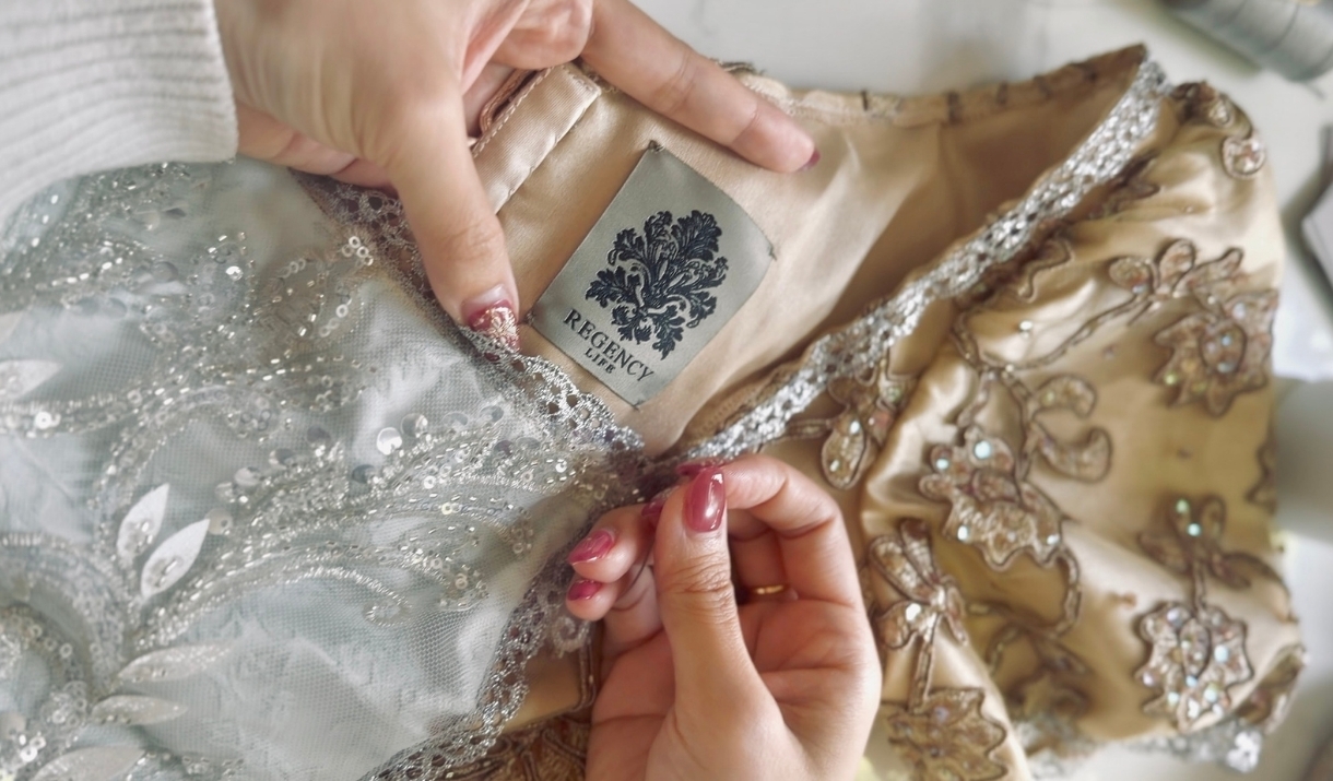Close-up of a garment label with the Regency Life logo, on an intricately beaded dress.