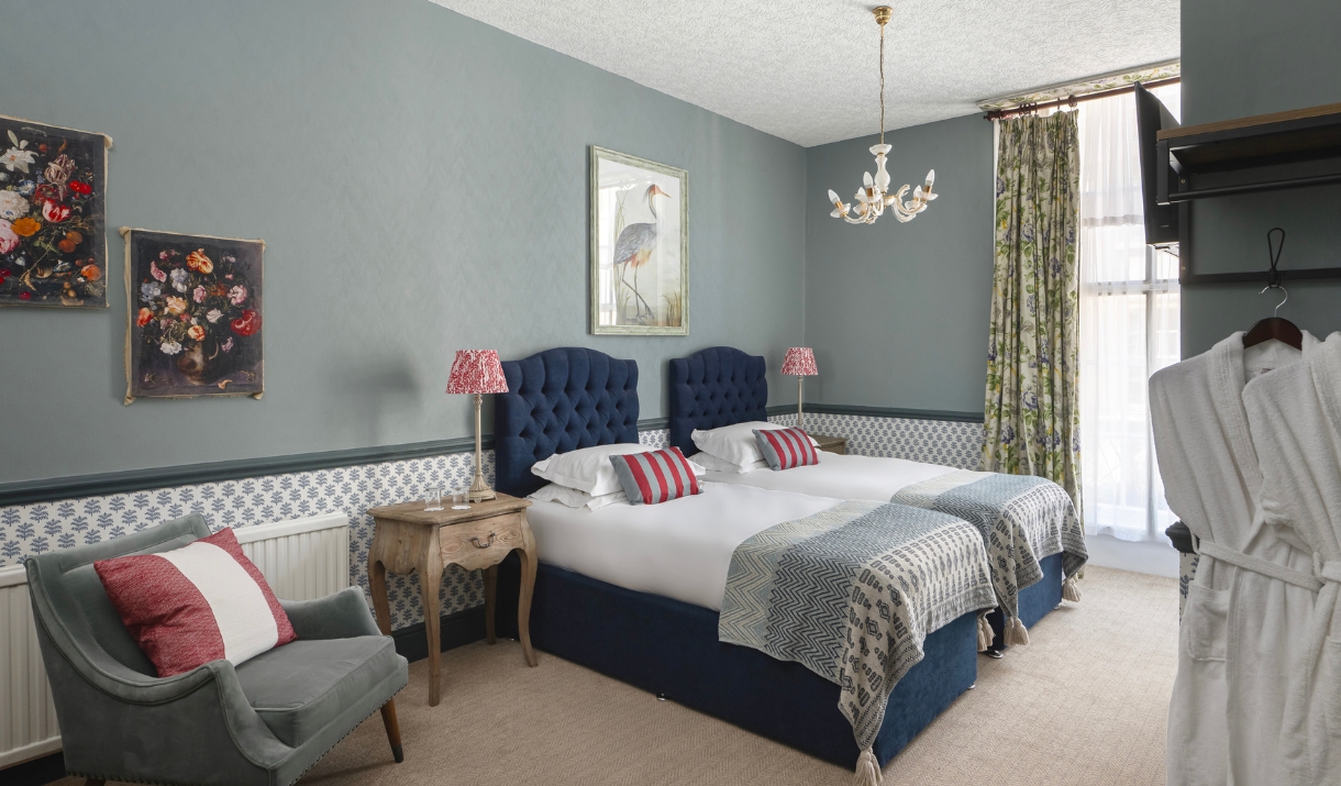 A Georgian style bedroom with grey blue tones and two dark blue single beds.