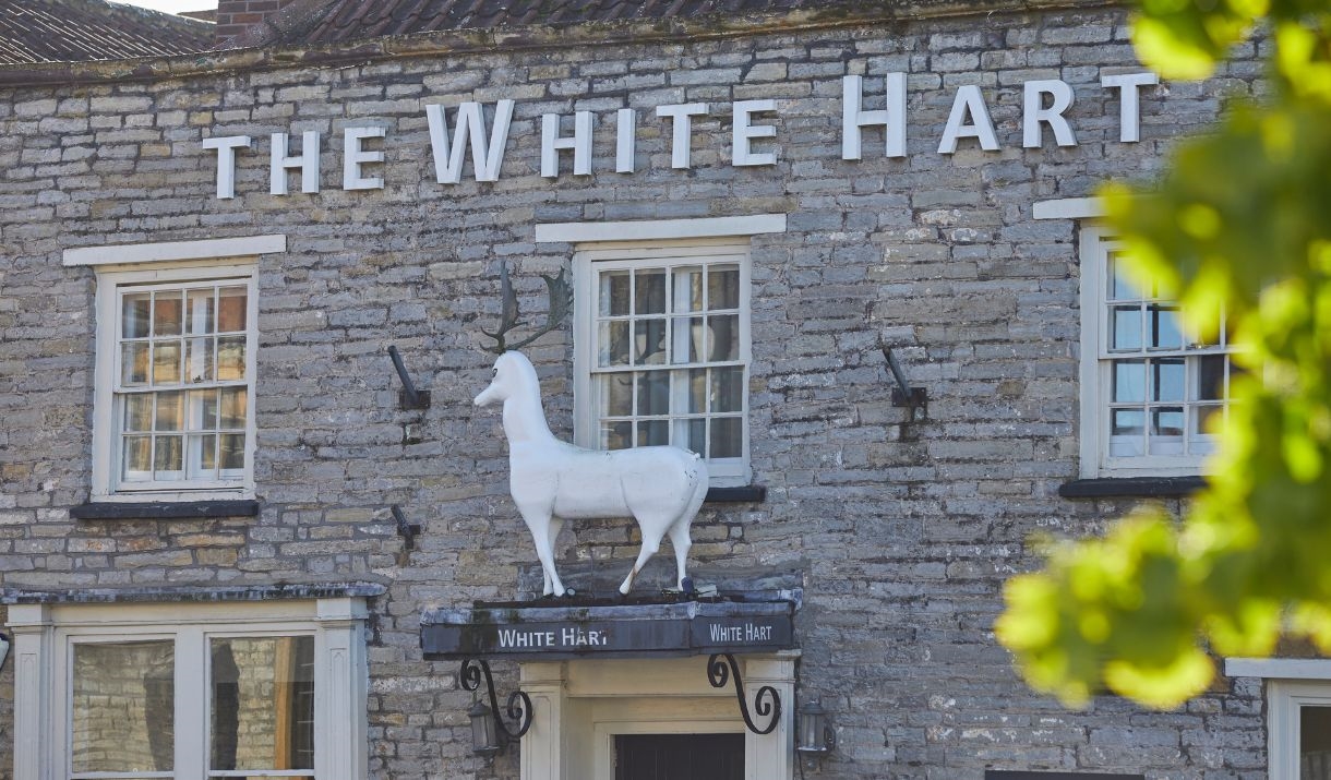 A stone building with The White Hart written on the front in white lettering and a large white stag statue above the door
