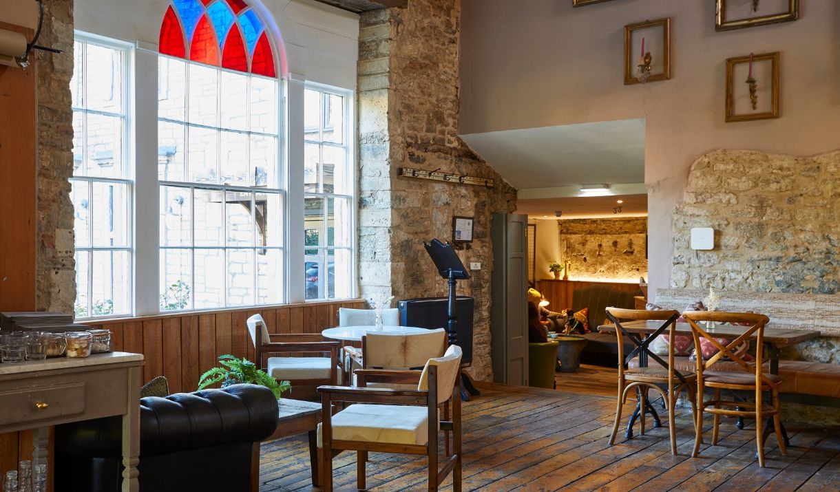 A room with white walls and exposed bricks, wooden floors, and wooden tables and chairs