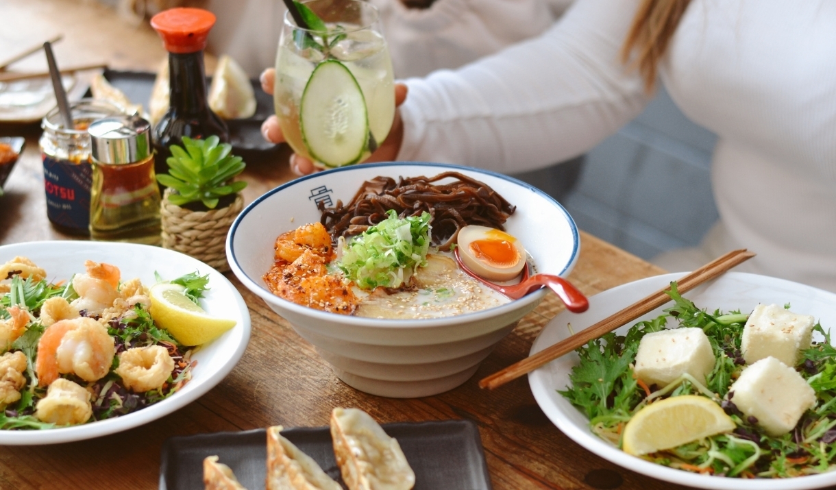 Various japanese dishes on a table: including a ramen bowl with an egg and meat, a prawn dish, and a salad.