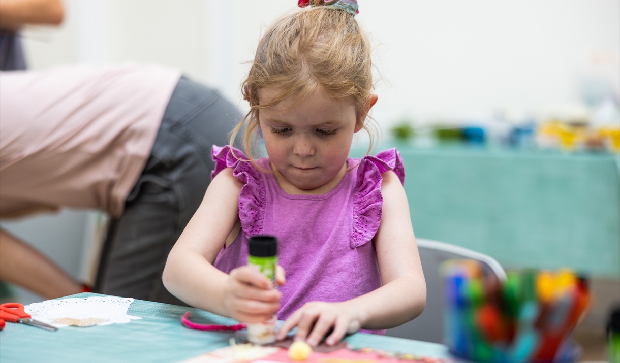 A young girl in a purple top making art with a glue stick