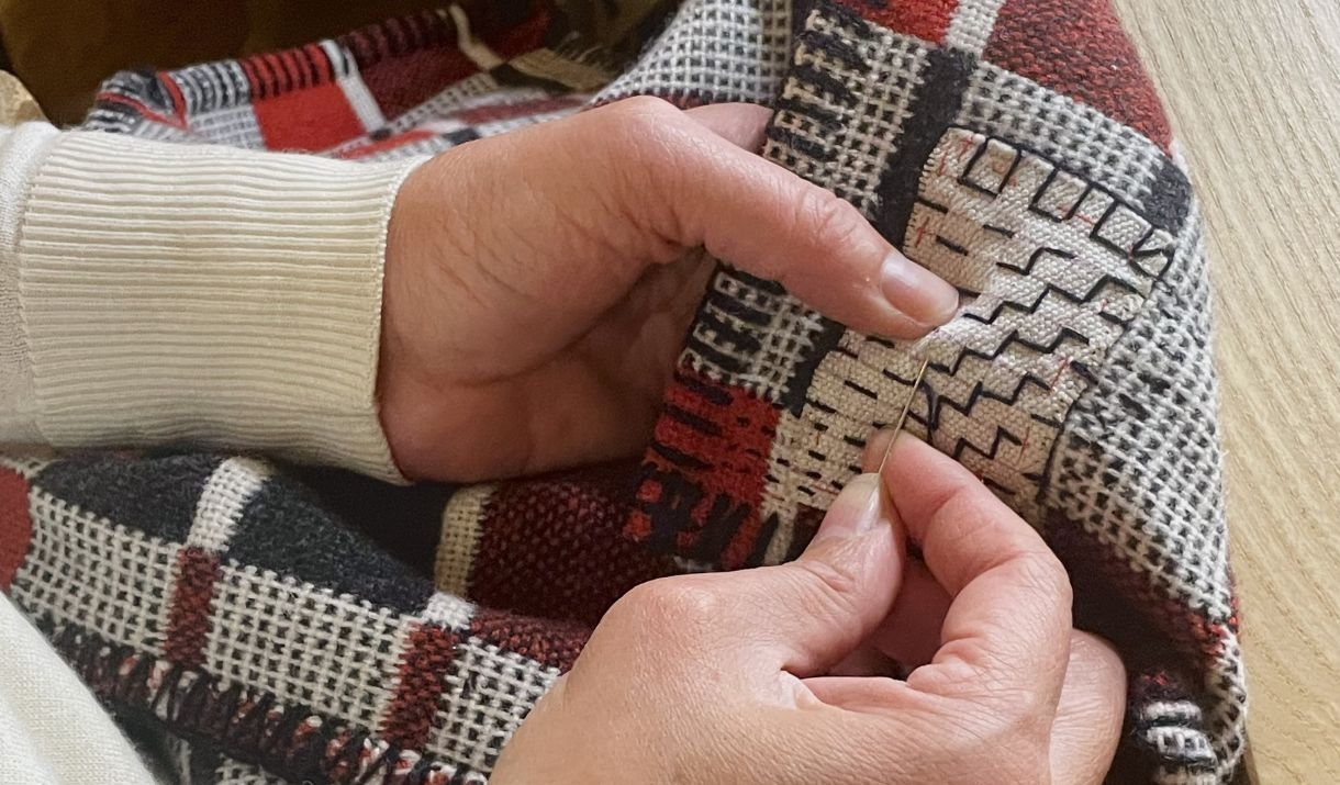 a pair of white hands mending a red black and white Welsh wool blanket with needle and thread