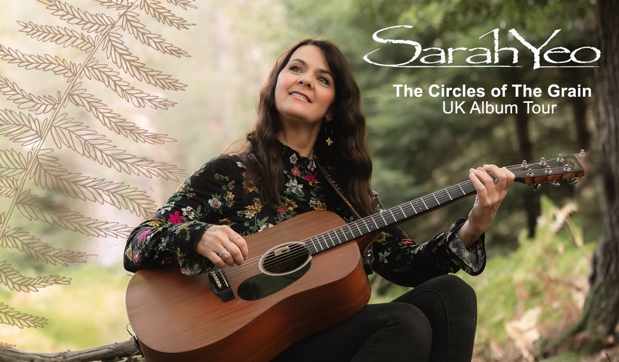sarah yeo sitting in the forest with her guitar