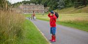 A child on the path outside Dyrham Park house looking through binoculars