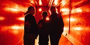 Three teenage girls face away from the camera in a corridor with red lighting.